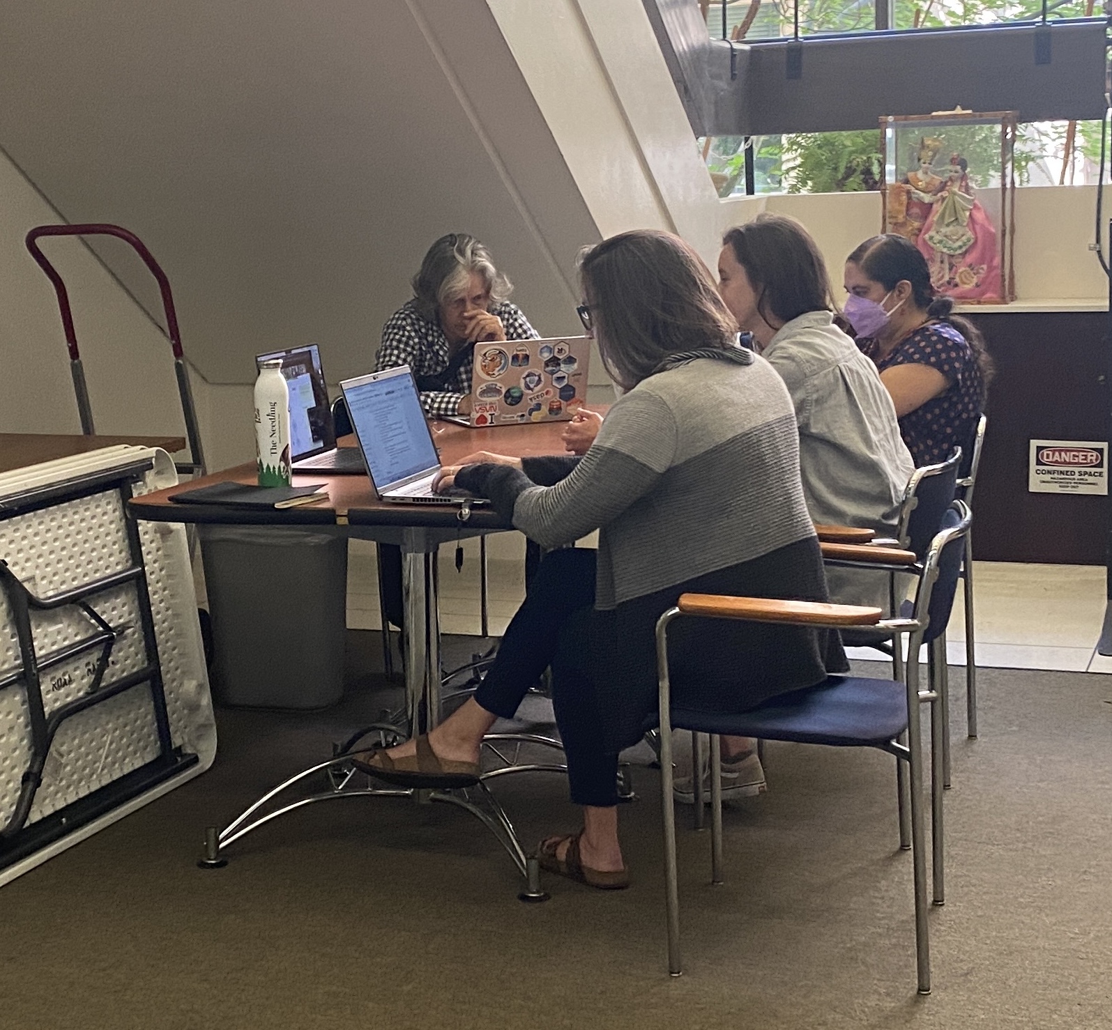 4 women sit around a table, concentrating with laptops open.